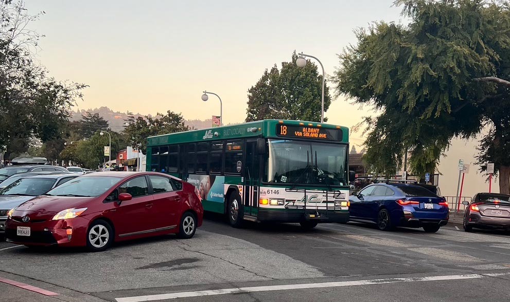 A photo of Solano Avenue demonstrating how crowded the street gets with a bus in one lane, a car passing in the other, and full parking leaving little extra space.